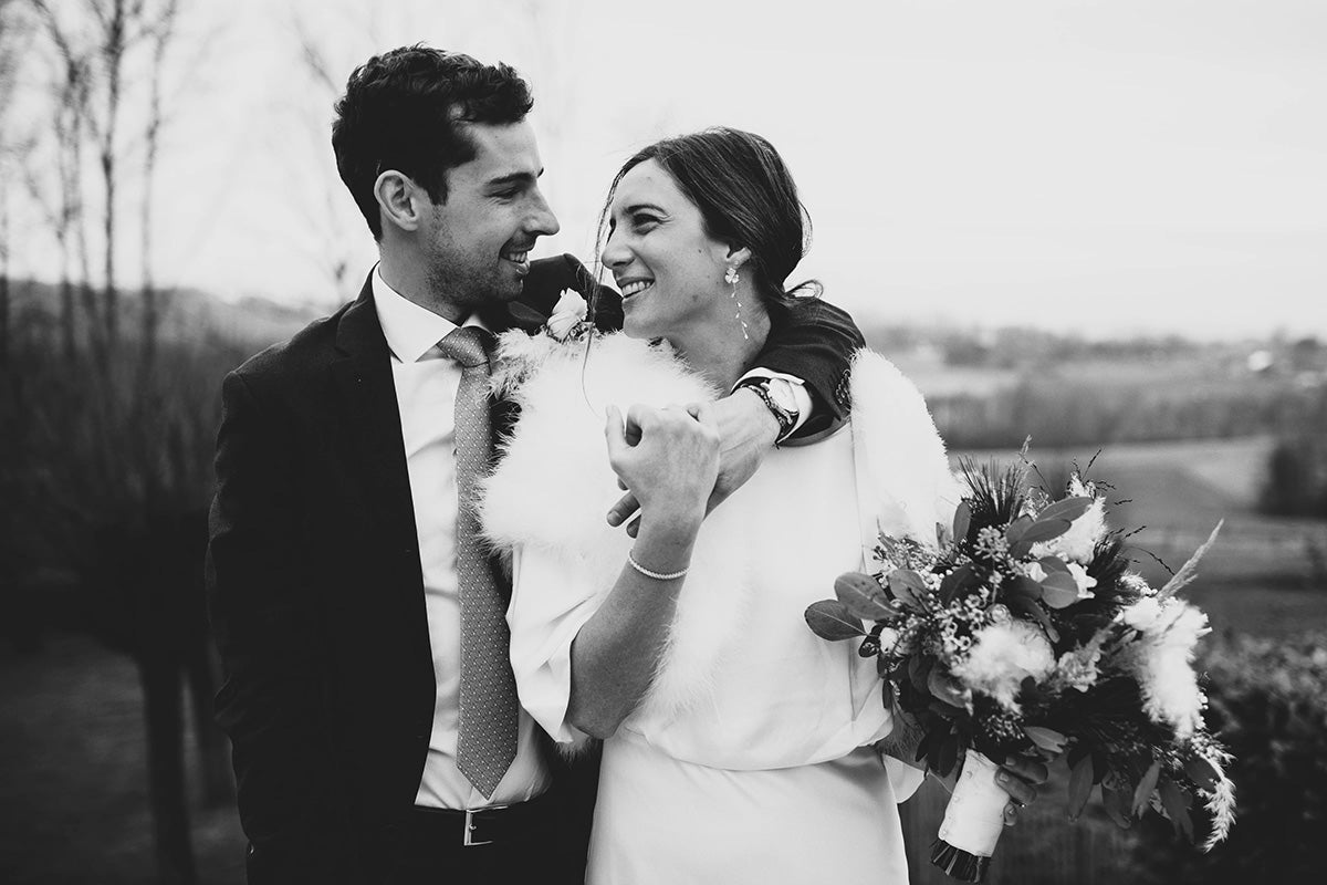 Mariées se tenant par l'épaule entrain de se regarder avec un bouquet à la fin et des boucles d'oreilles longues à fleurs