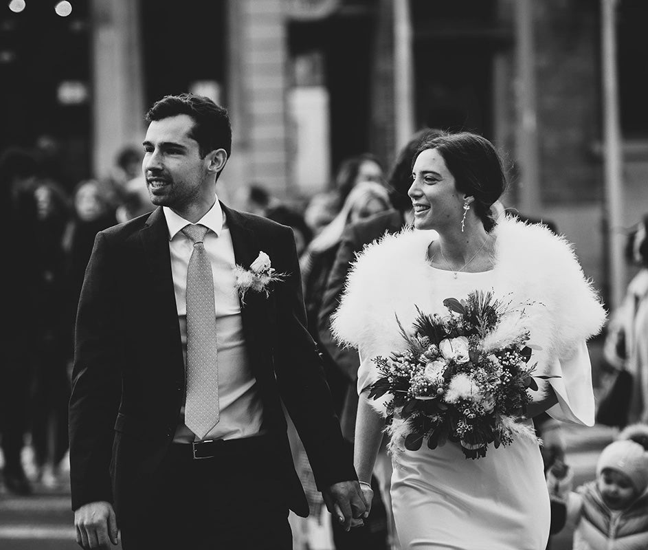 Mariée marchant dans la rue avec l'homme en costard et la femme avec une robe blanche et un gilet à poil doux