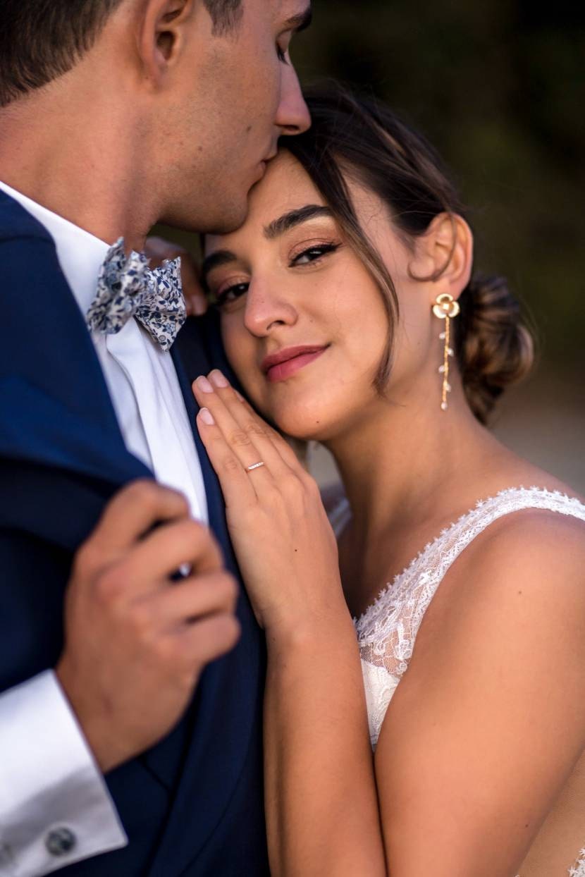 mariée qui se tiens contre son mari avec des boucles d'oreilles à fleurs longue et dorés