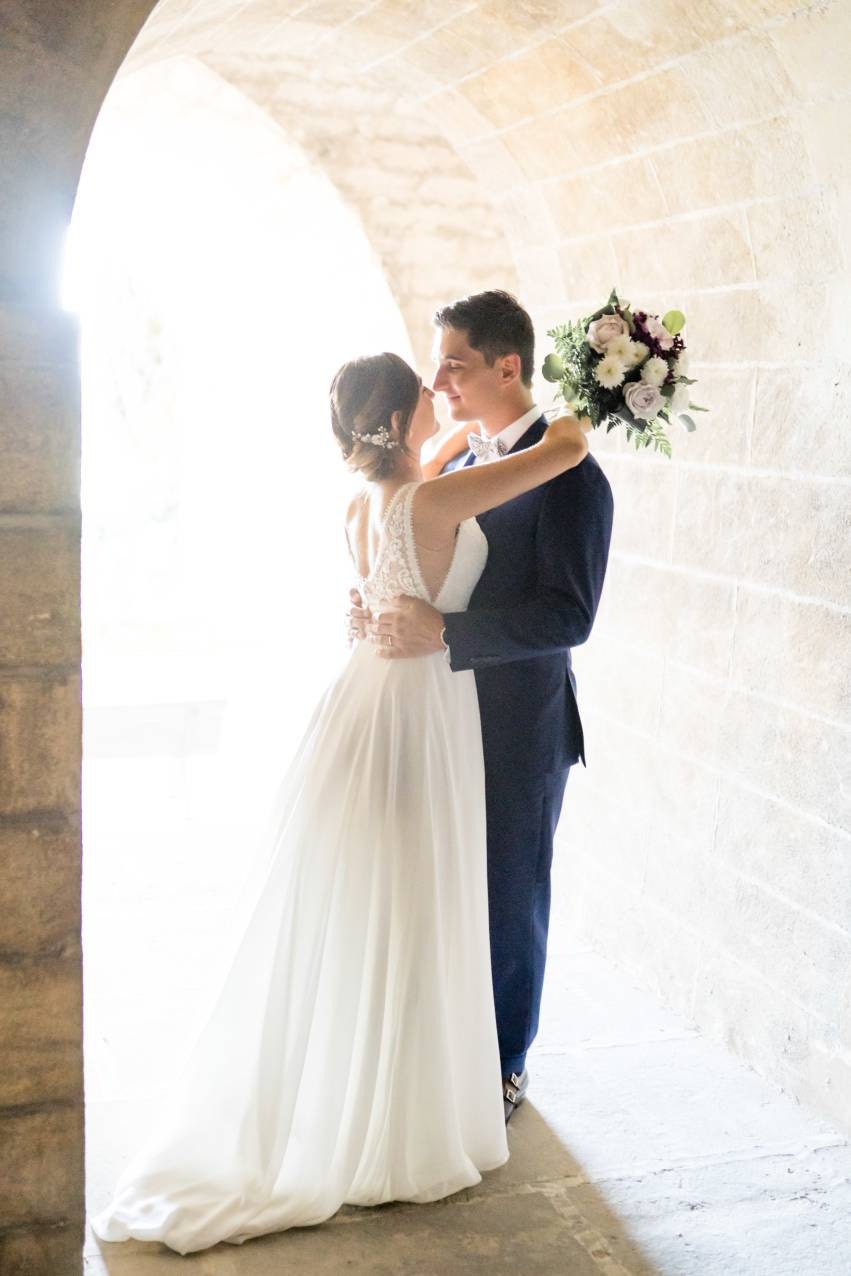 Recém-casados ​​em um túnel de pedra com um vestido longo branco e um buquê de flores cor de rosa