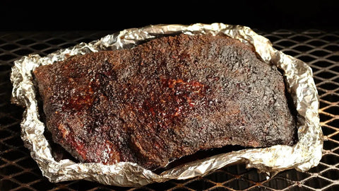 Downward view of a brisket covered in sauce, nestled in a tinfoil boat, cooking on a Yoder Smoker, absorbing smoky flavors.