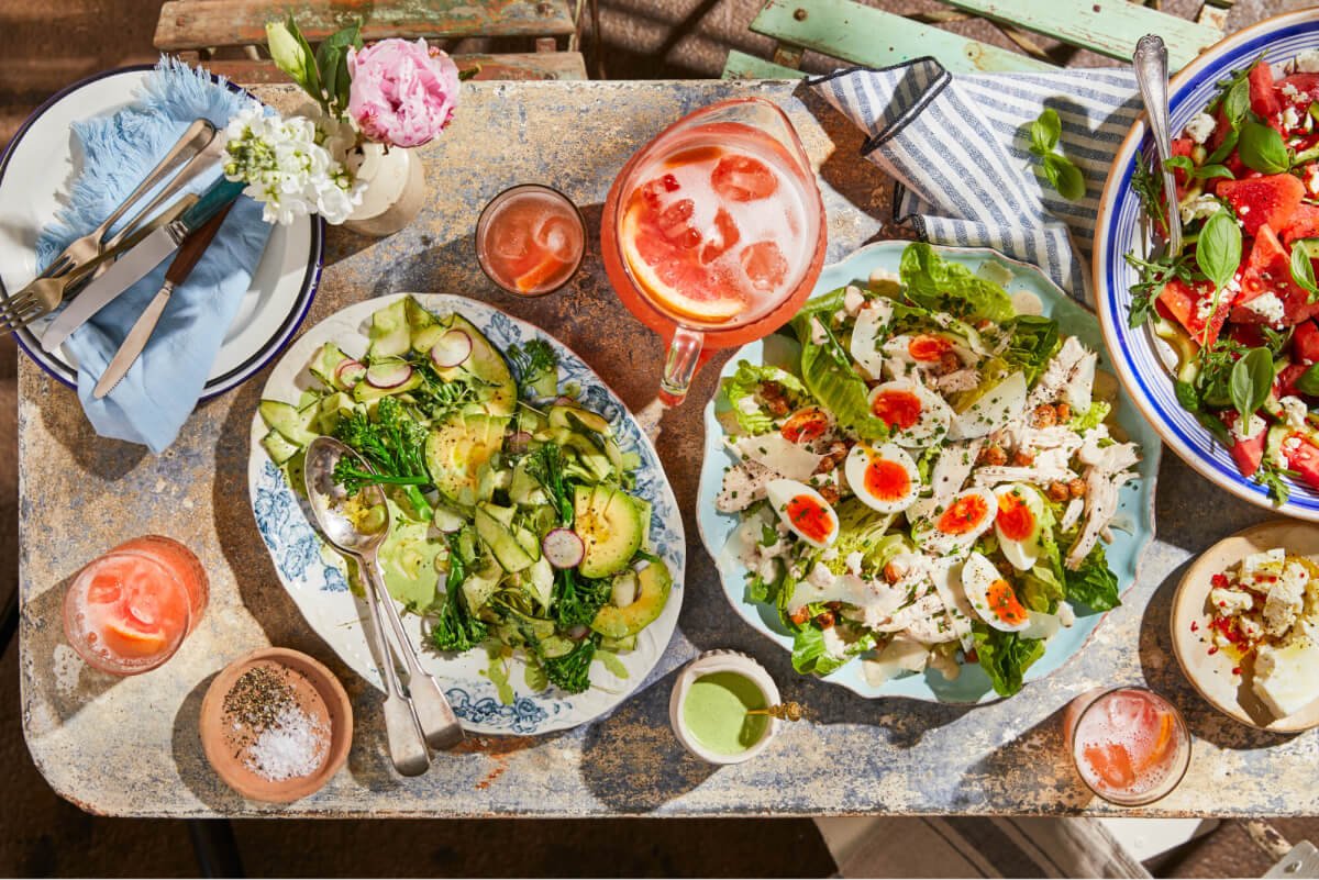 Alfresco summer salads arranged outside on a table with summer crockery and a grapefruit cocktail jug