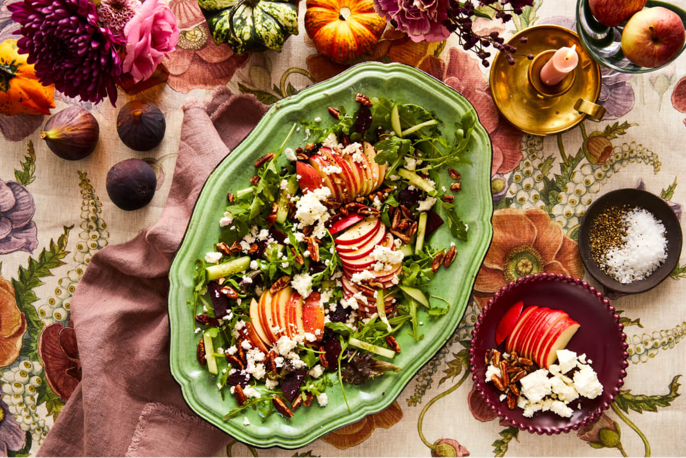 Apple and feta salad in a beautiful green serving platter on an autumnal table with purples, greens, orange, pink