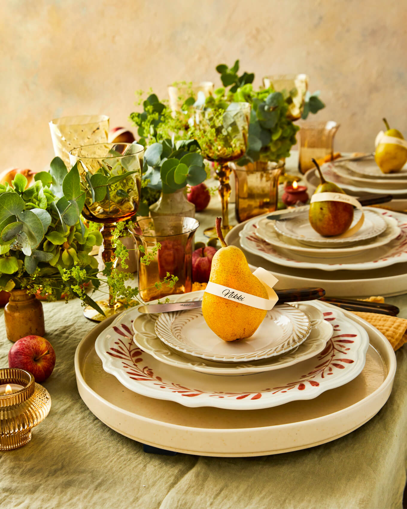 Autumnal place settings on a rustic table setting with pears, layered plates and herbs, green, orange, brown, cream