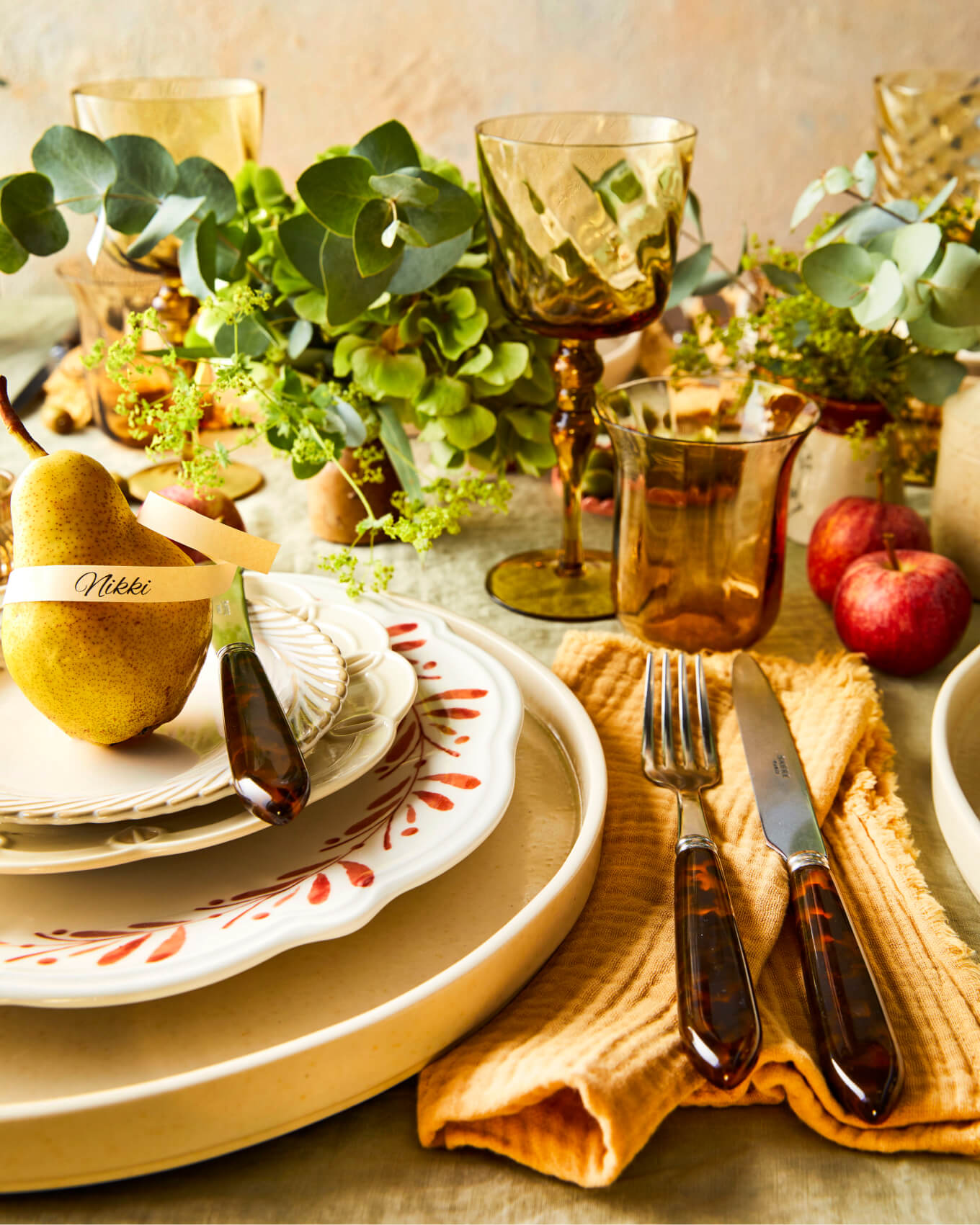 Close up of an autumnal place setting with pears, layered plates, orange, brown and green