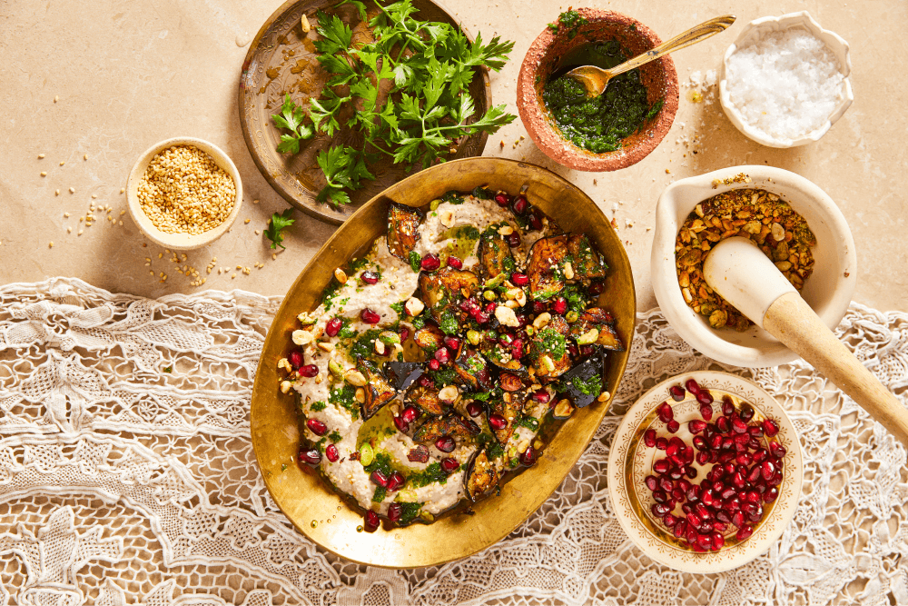 Baba Ganoush dip in a gold serving dish with pinch pots fo toppings on a table