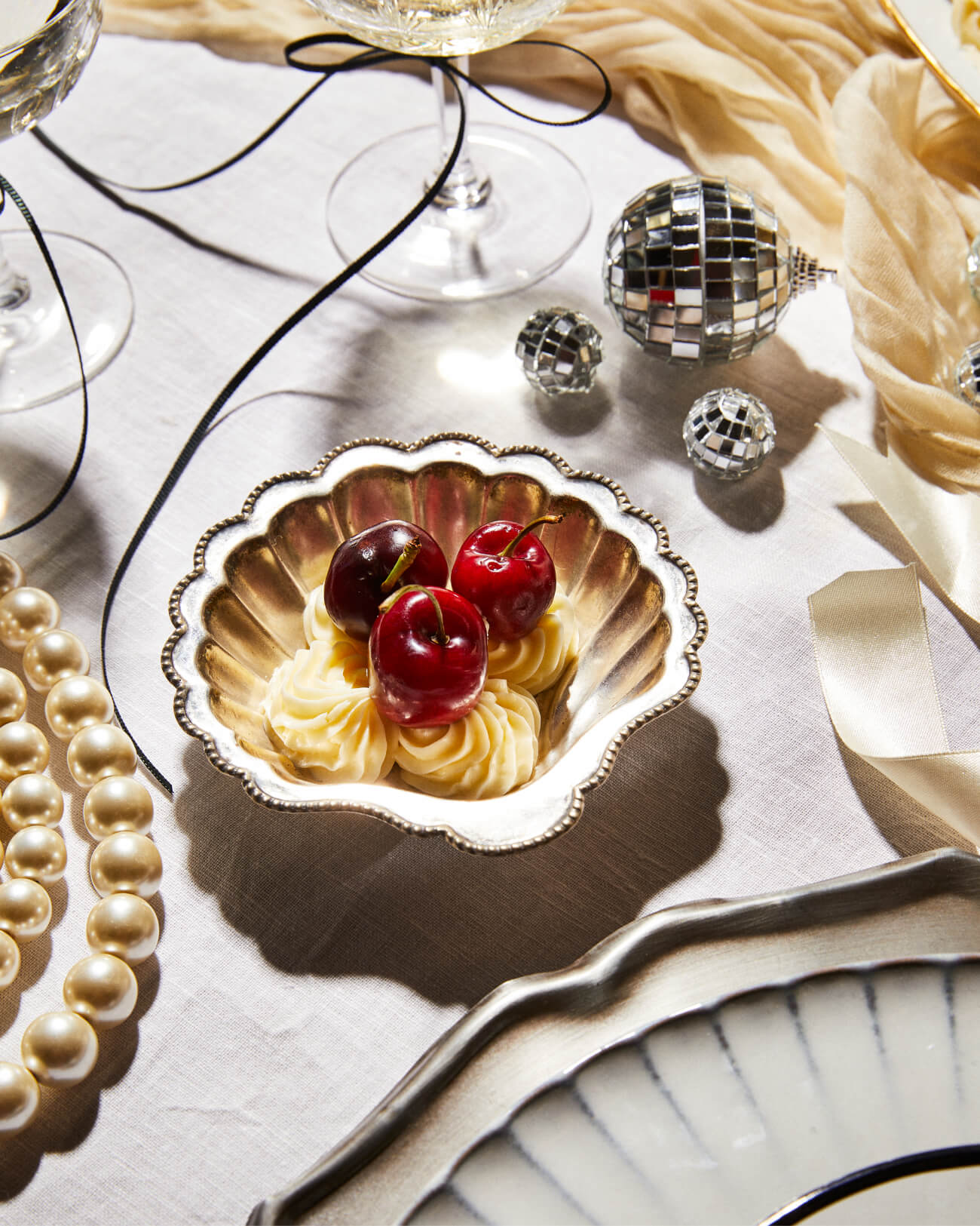 New Year's Eve table from The Social Kitchen with vintage silver shell bowl, disco balls, vintage pearls and champagne glass tied with black ribbon