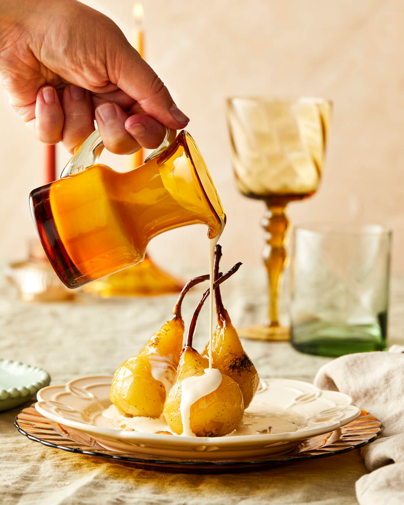 poached pears on a beautiful table setting with a jug of cream being poured over the top