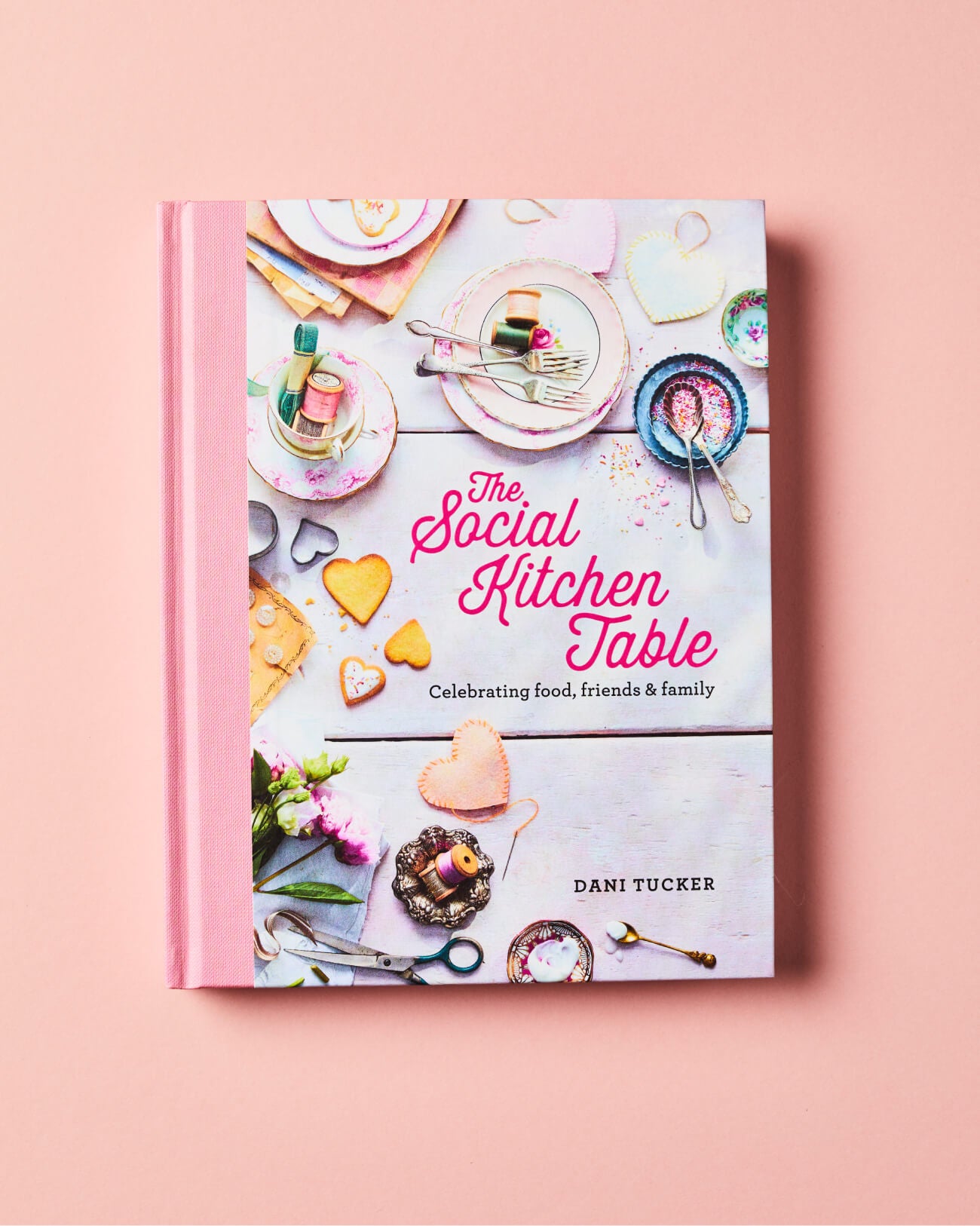 The Social Kitchen Table Cookbook by Dani Tucker on a pink background