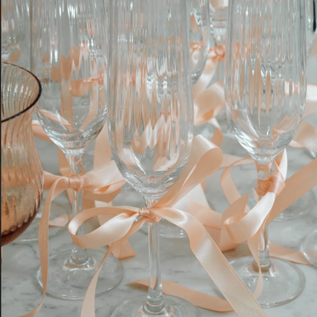 Beautiful clear champagne glasses with peach ribbon. The Social Kitchen studio