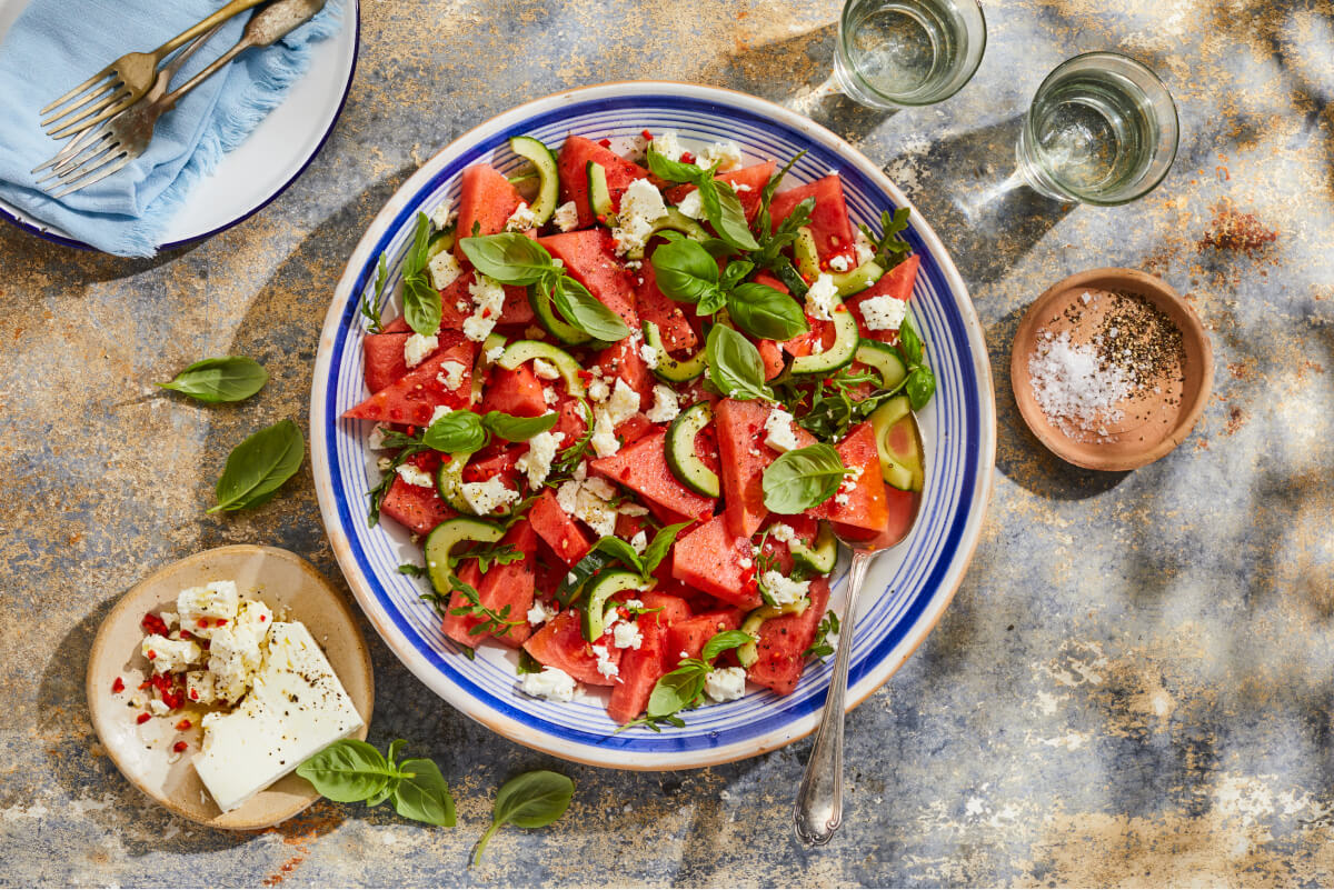 Watermelon and feta salad with basil leaves served in a blue and white summer salad bowl