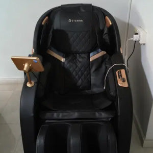 A black and gold massage chair with a small attached monitor and remote control.