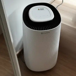 A white air purifier placed on a wooden floor next to a wall.