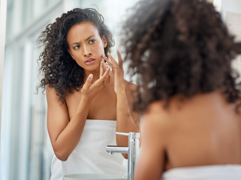 woman with adult acne looking in mirror