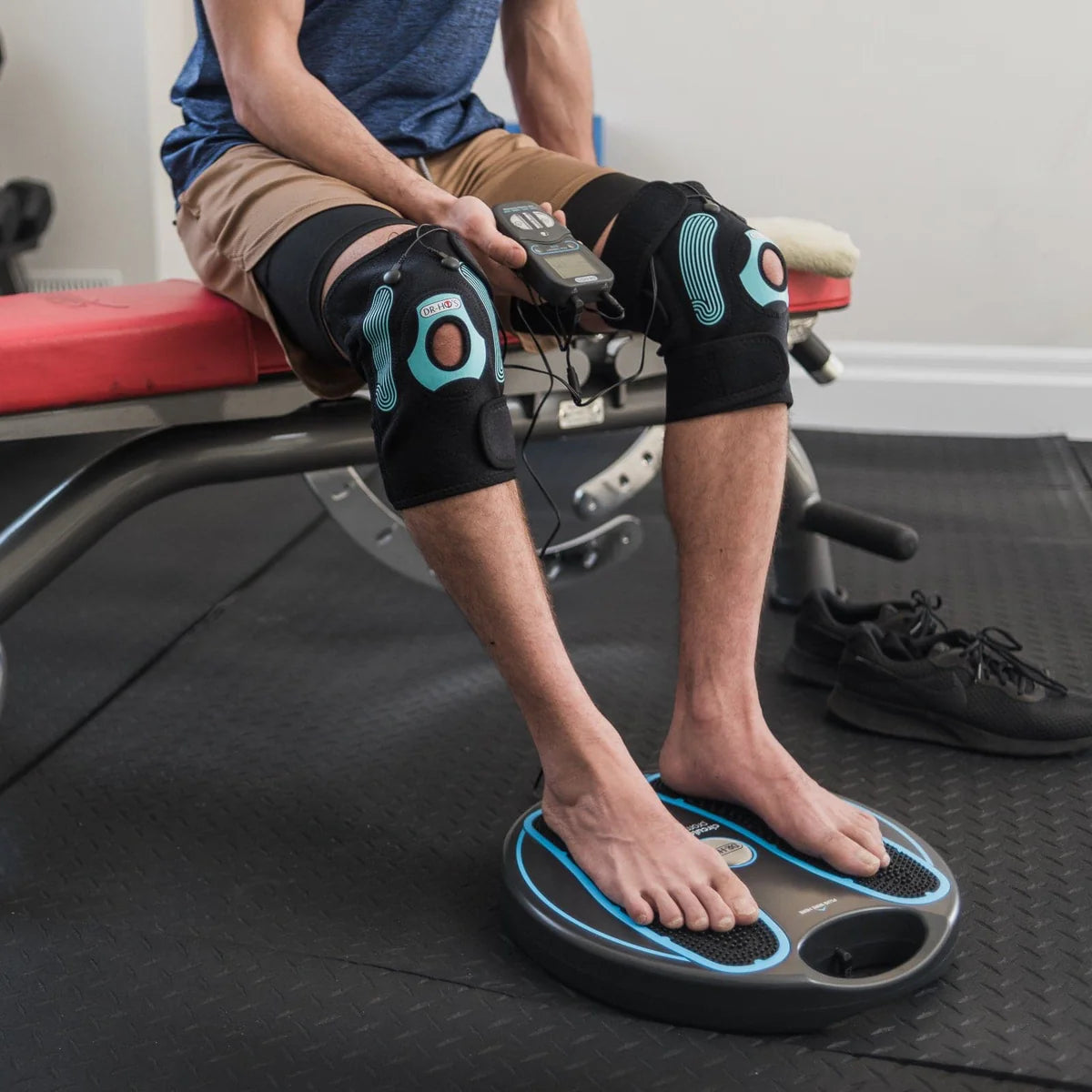Man using knee braces and foot massager on a gym bench.
