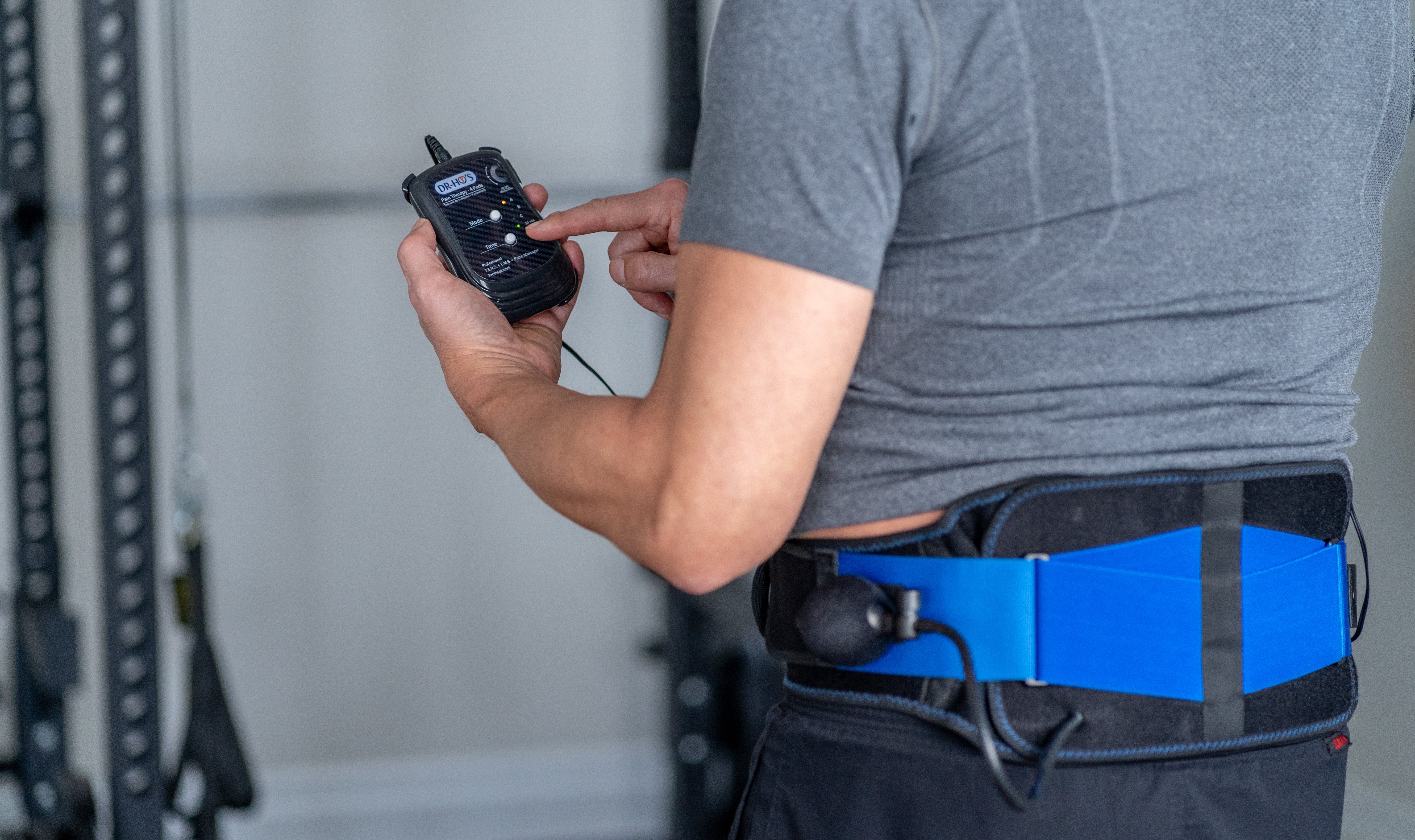 Person adjusting settings on a handheld device while wearing a back support belt.