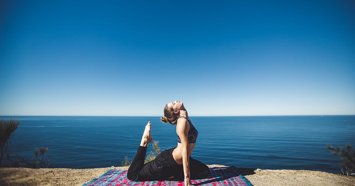 A woman doing yoga by the ocean.