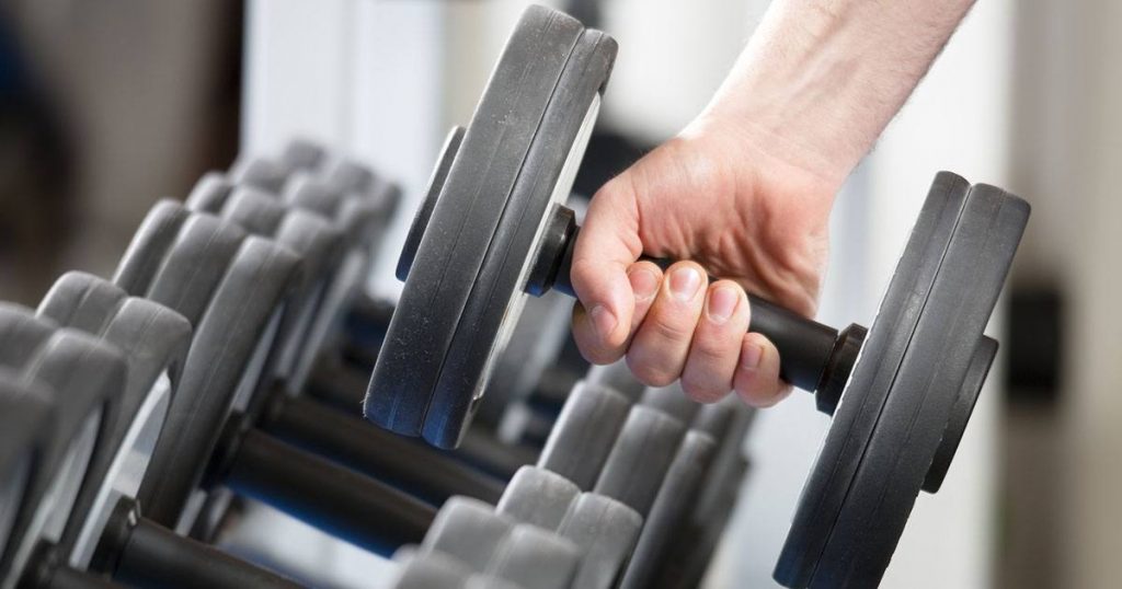 A person holding a dumbbell in a weight room.