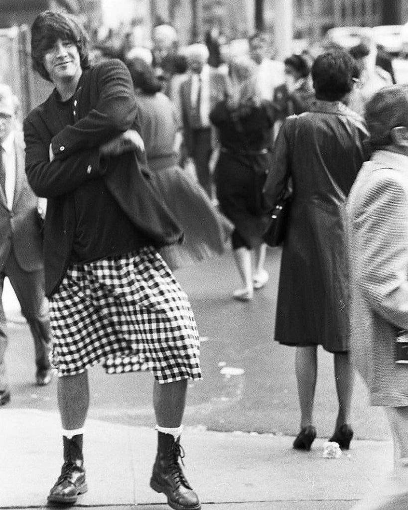 Keanu Reeves in Toronto, Ontario, with arms crossed, in black suit jacket and plaid skirt, smiling.