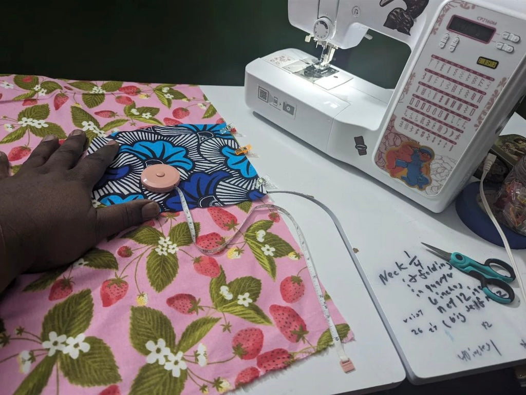 Hand, on pink and green strawberry print fabric, on a table, next to sewing machine.