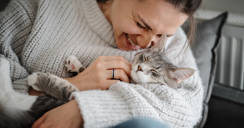 Mujer acurrucando a su gato gris en brazos, sonriendo.