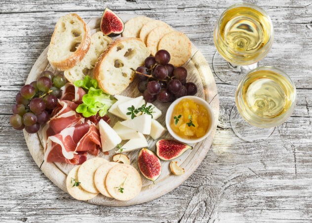 Pair wine with brunch – top-down view of a small breakfast cheese platter with fruit, nuts, and two glasses of white wine