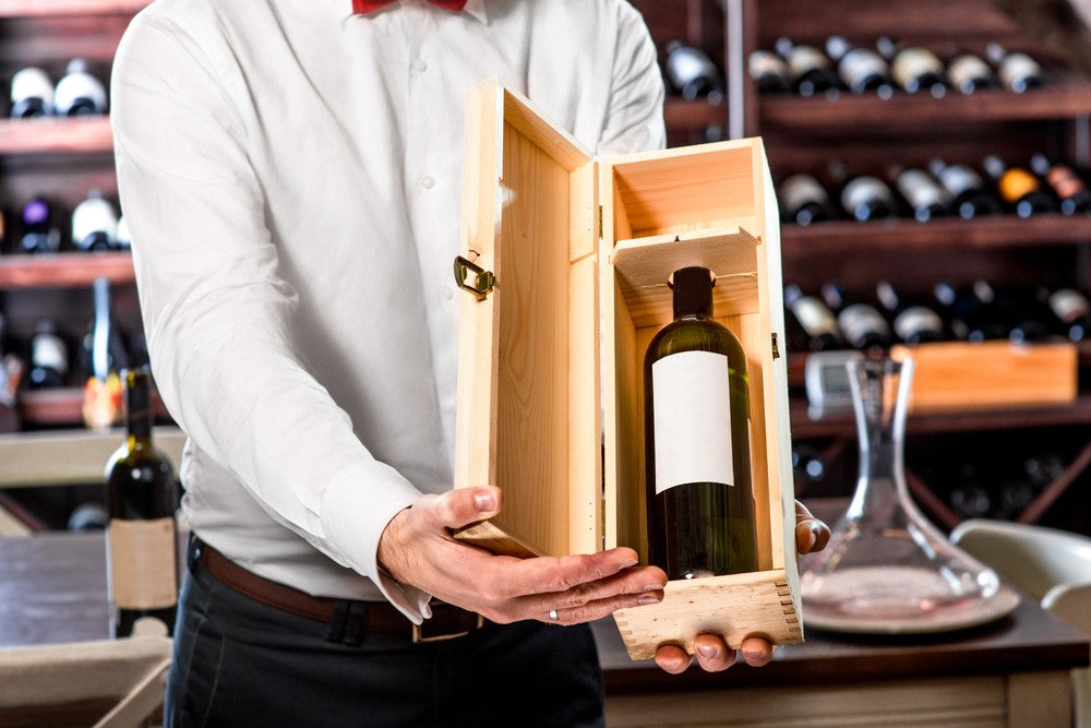 Sommelier wine expert shows expensive wine in wooden box to viewer for consideration.