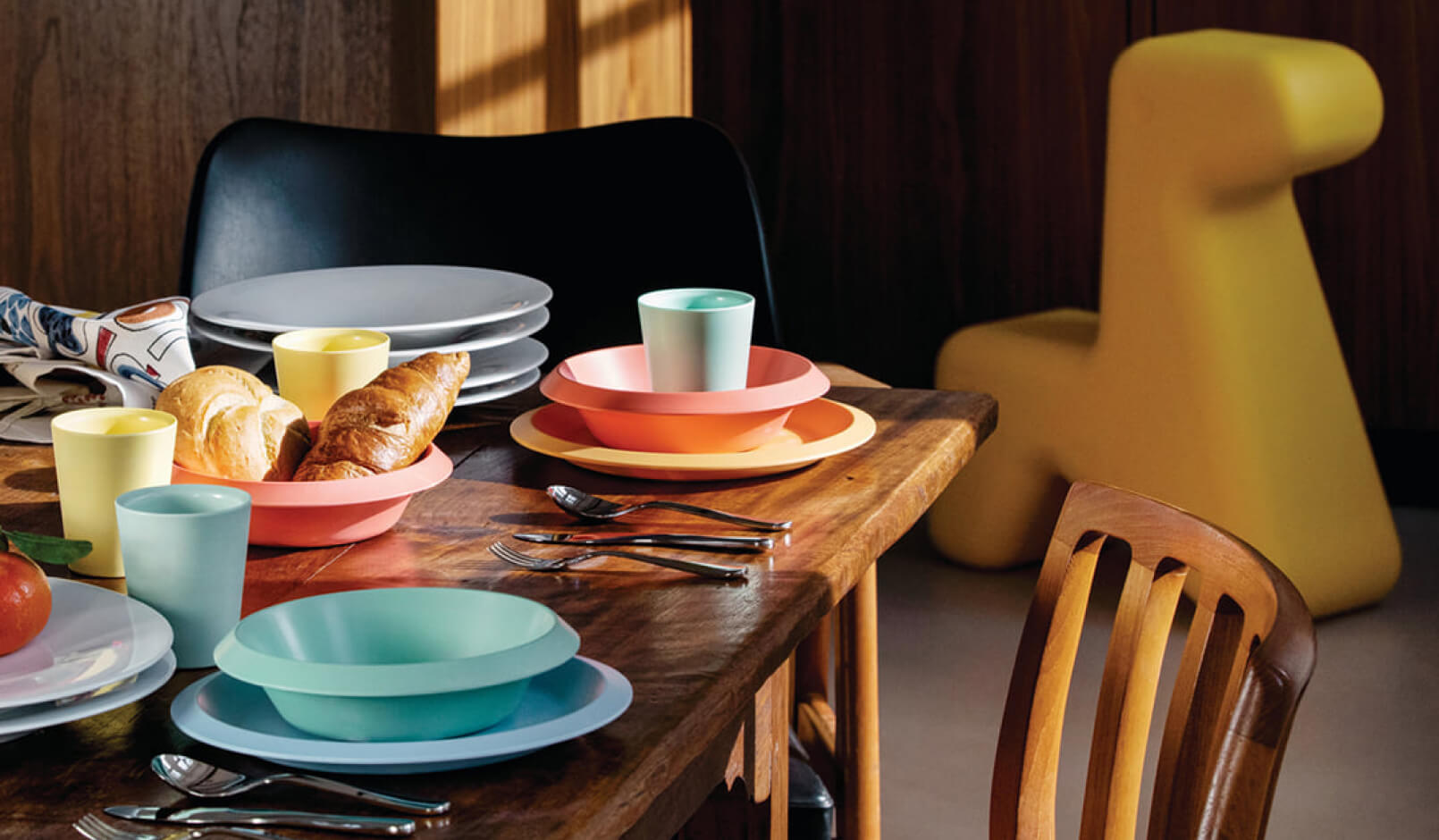 Wooden table with plates, cups and bowls in pastel colors.