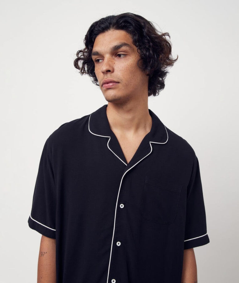 A man wearing a black button up short sleeve shirt with white detailing.