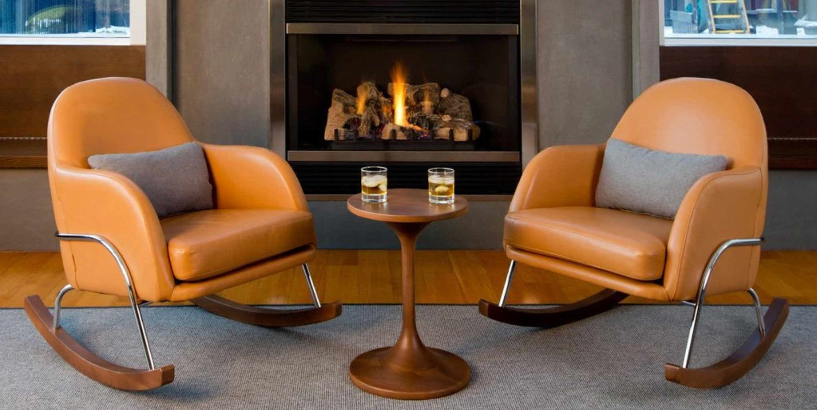 Two modernly designed brown leather rocking chairs sit comfortably in front of a fireplace. Two glasses of scotch on the rocks sit on a table in between.