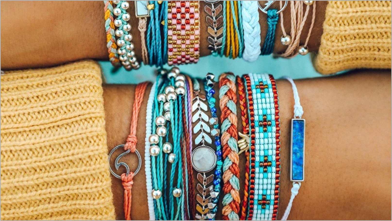A close up of a woman’s arms wearing several Pura Vida bracelets