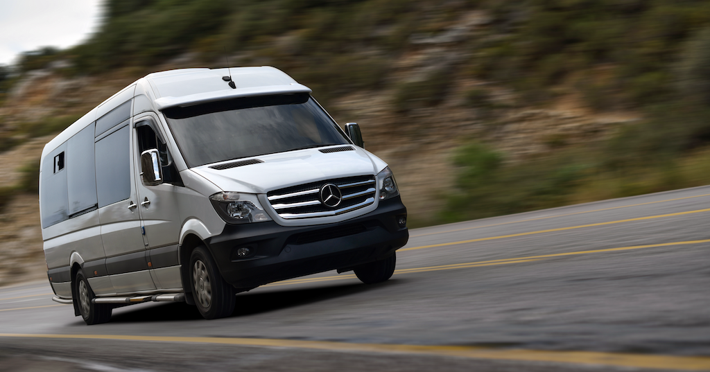 Top-heavy Mercedes Sprinter Van Driving Down Road with Timbren Helper Springs