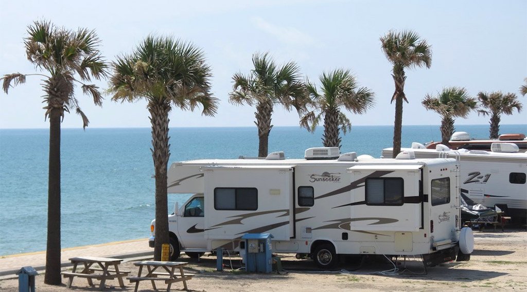 Mobile homes garés parmi les palmiers au parc de camping-cars avec vue sur l'océan