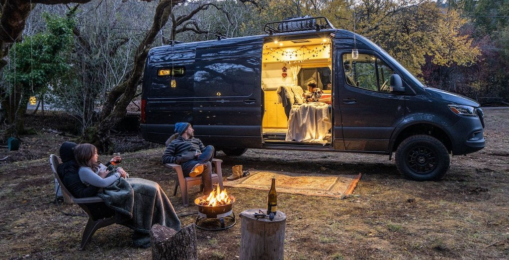 Family sitting outside their Sprinter Camper Van around a fire