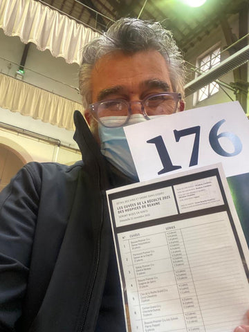 Roberto Cipresso wearing a mask inside a hall holding up an auction lot list and a bidding paddle labeled "176"