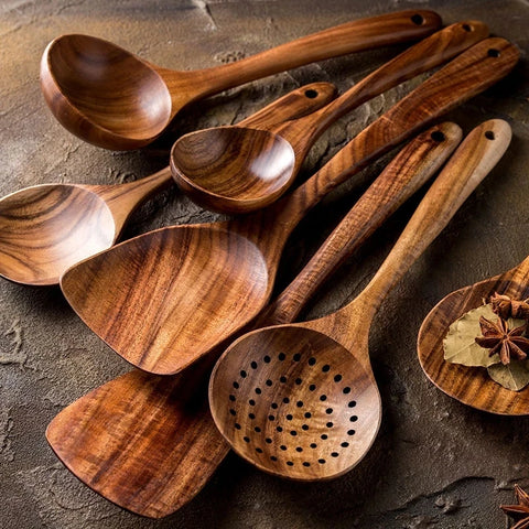 Seven wooden kitchen utensils, including spoons, a ladle, a skimmer, and spatulas, arranged on a textured surface with spices.