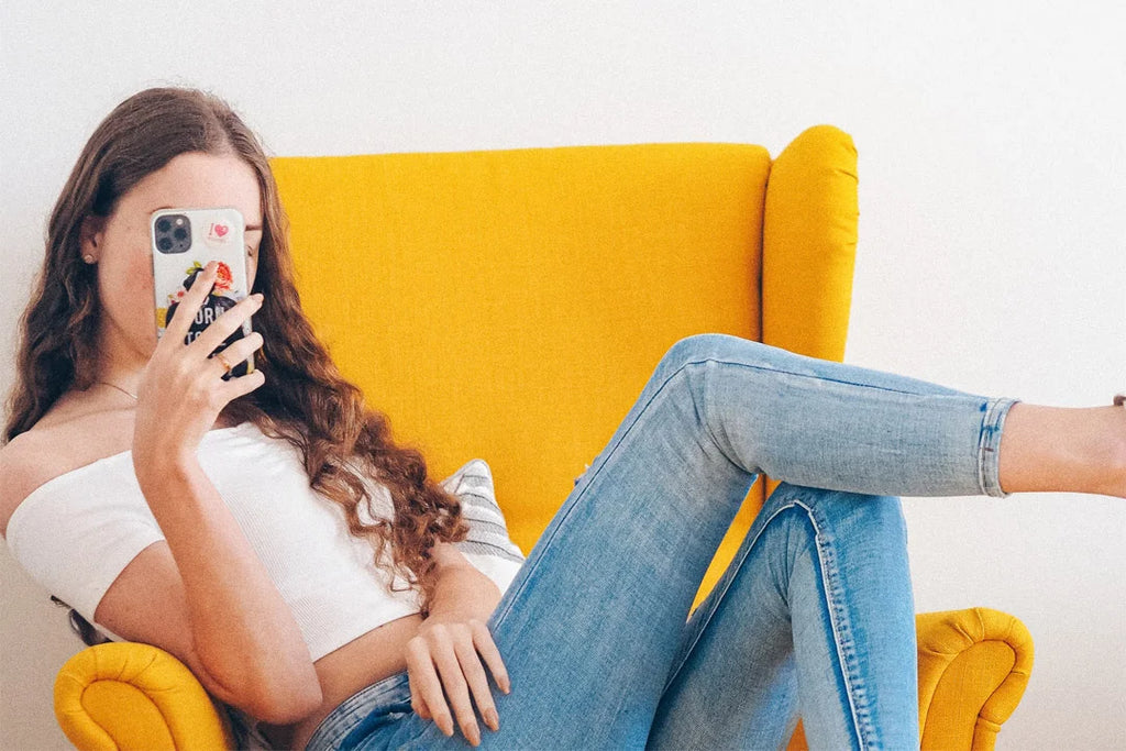 A photo of an influencer sitting in an orange chair taking a photo with her phone