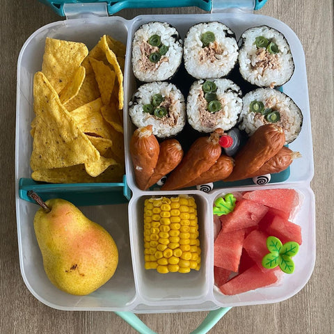 an open bento box with sushi rolls, chips, a pear, corn, and watermelon