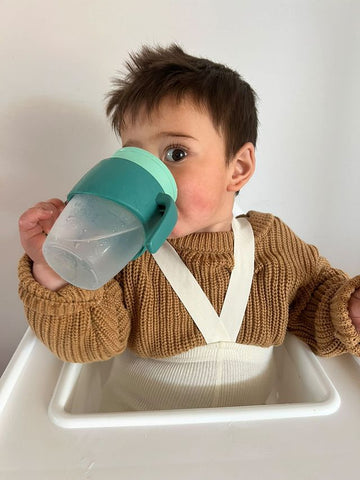 a little boy drinks from a 360 cup while looking at the camera