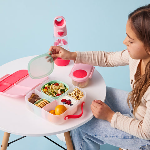 a school-aged girl sits at a table with a pink, non-toxic bento box filled with food