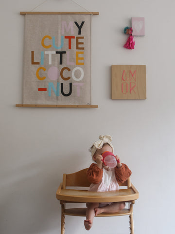 an infant in a high chair drinks from a 360 cup against a decorated wall