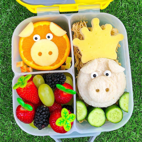 an open b.box bento box with a sandwich shaped like a pig's face and an orange shaped like a pig's face
