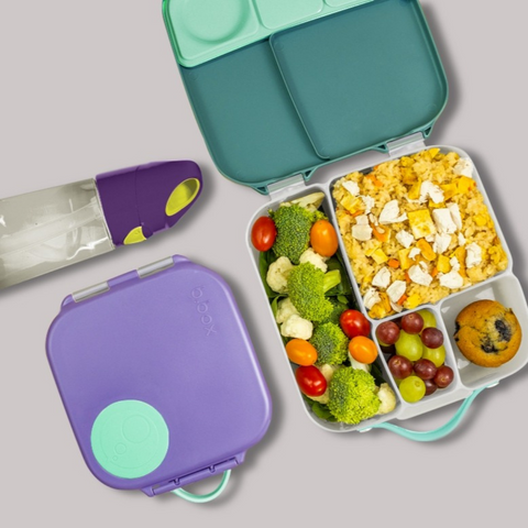 purple and green b.box lunch box containing chicken fried rice, grapes, assorted vegetables, and a muffin