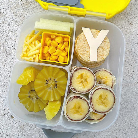 a b.box mini lunchbox featuring all yellow foods, like banana roll-up, pineapple, potato straws, and corn