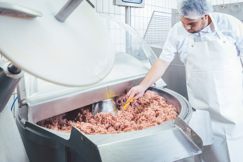 A butcher checking the mince in an industrial, floor-standing meat grinder