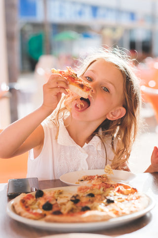 Hungry kid girl eating pizza on cafe terrace on sunny day. outside restaurant