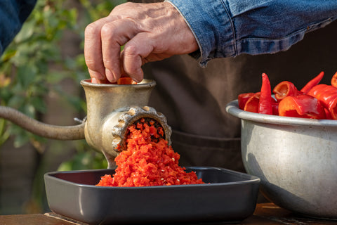 Red chilies being minced by a hand-cranked meat grinder