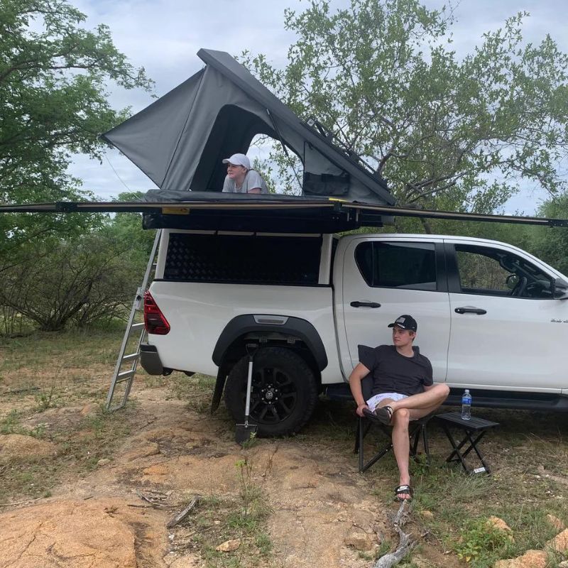 eezi-awn-blade-40th-edition-hard-shell-roof-top-tent-open-side-view-on-vehicle-with-persons-and-awning-in-nature