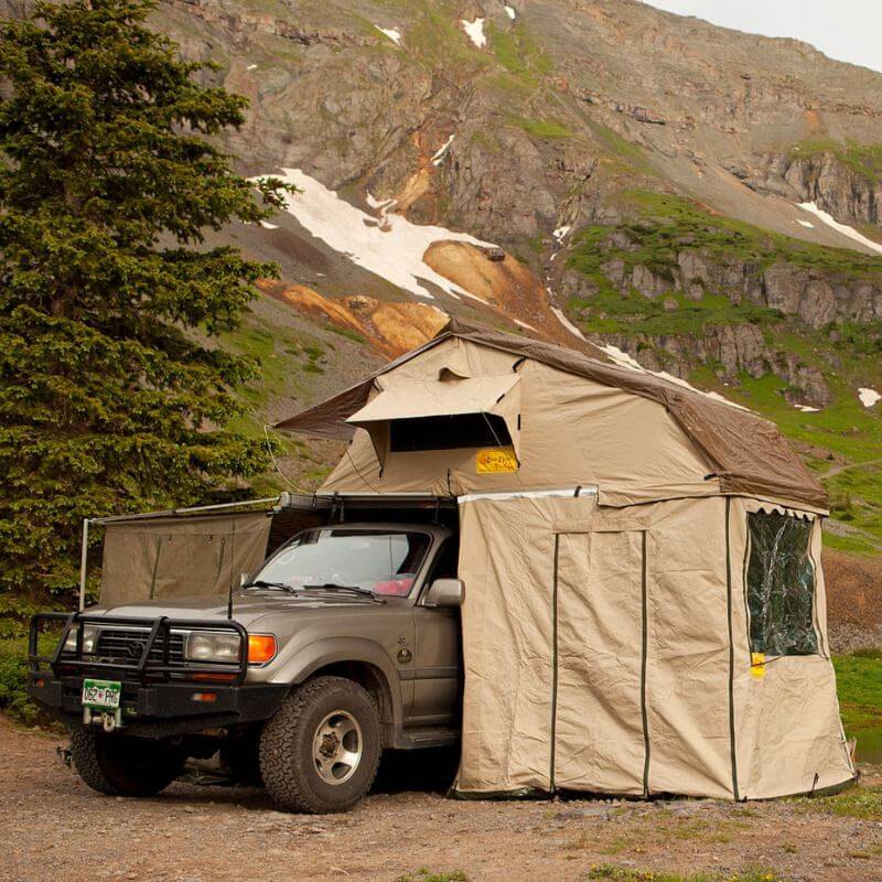 eezi-awn-xklusiv-soft-shell-roof-top-tent-beige-open-front-corner-view-on-vehicle-with-extended-room-and-big-windows-in-nature