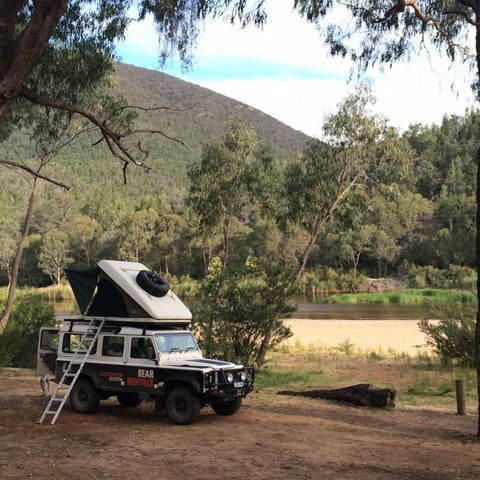 open-road-overland-land-rover-defender-with-hard-shell-roof-top-tent-open-front-corner-view-on-river-bed